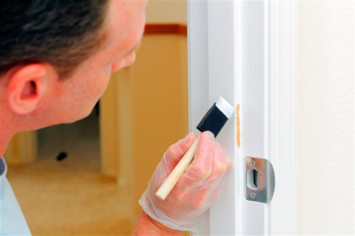 man with a small foam paint brush touching up wall with white paint