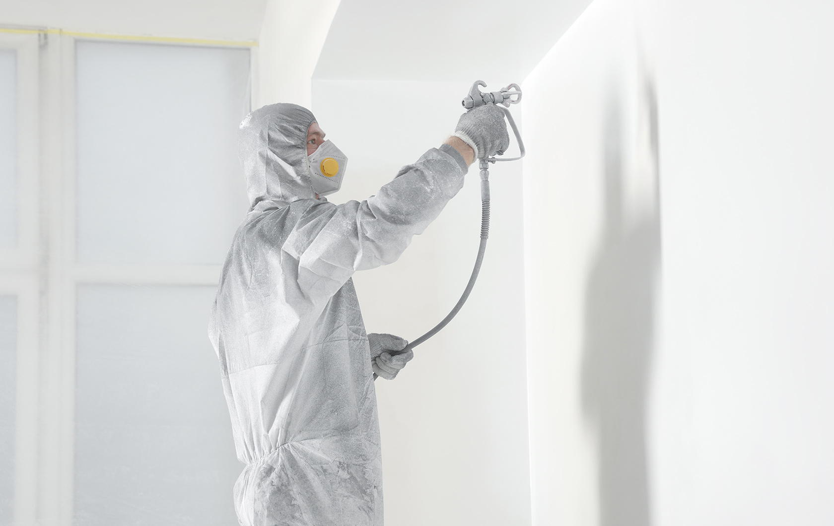 man spray painting a wall wearing a white protective suit and face mask