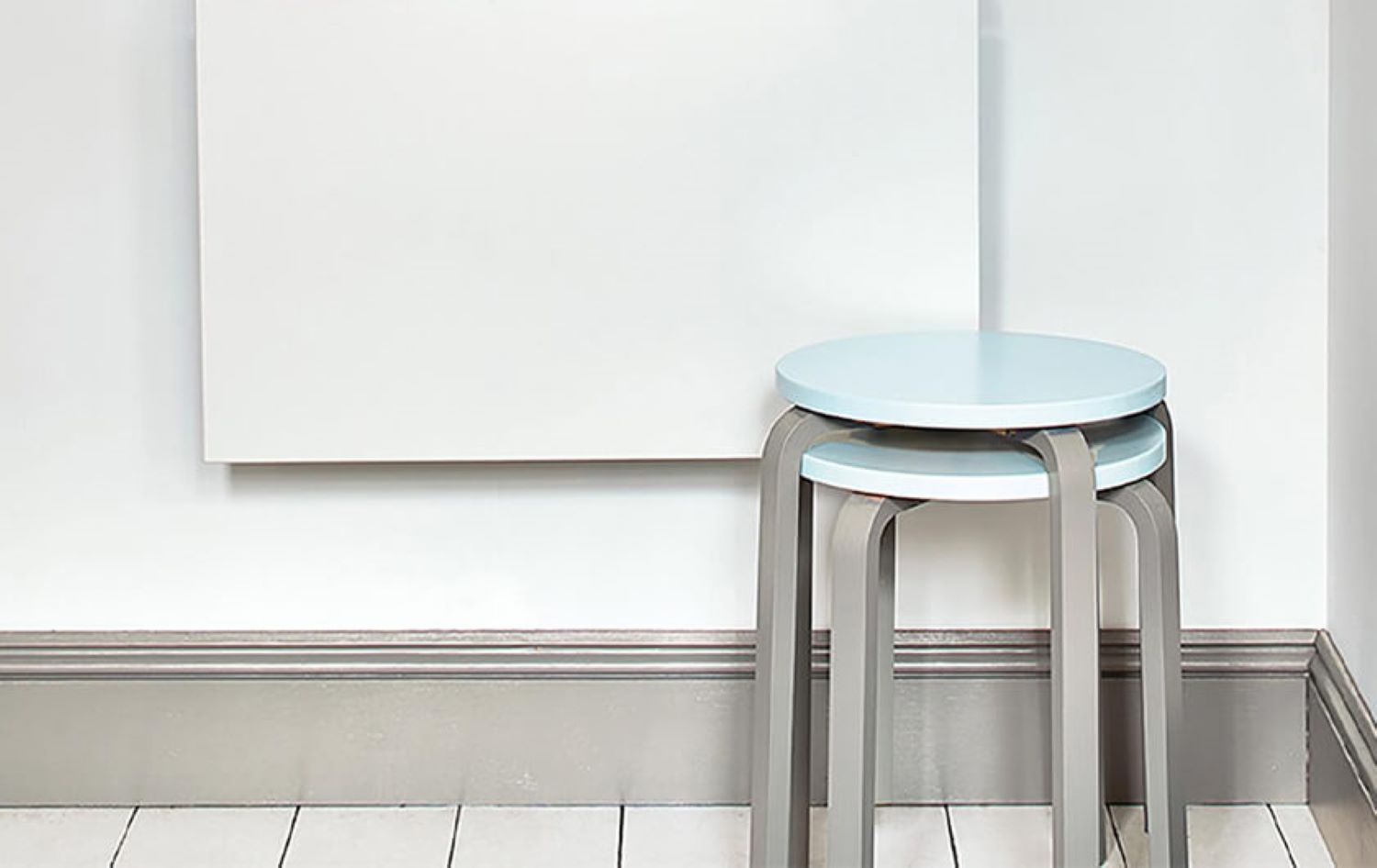 grey skirting board with white walls and two light blue stools stacked