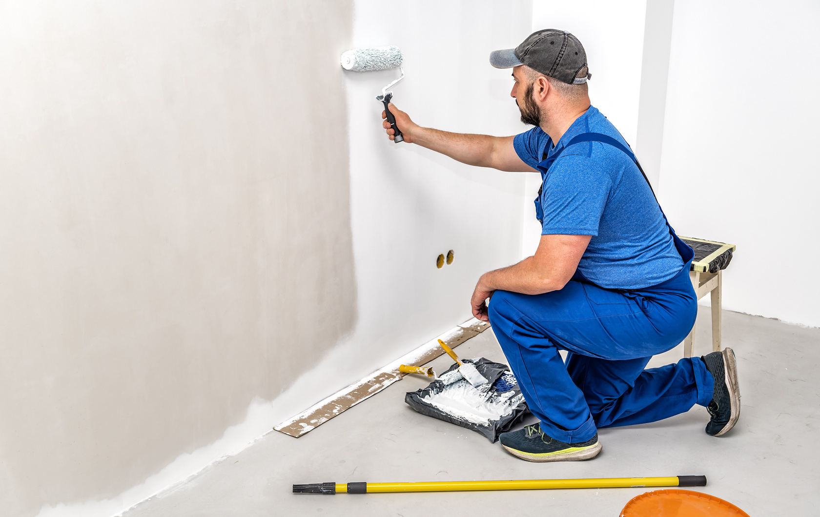 man painting a wall in white paint with a roller