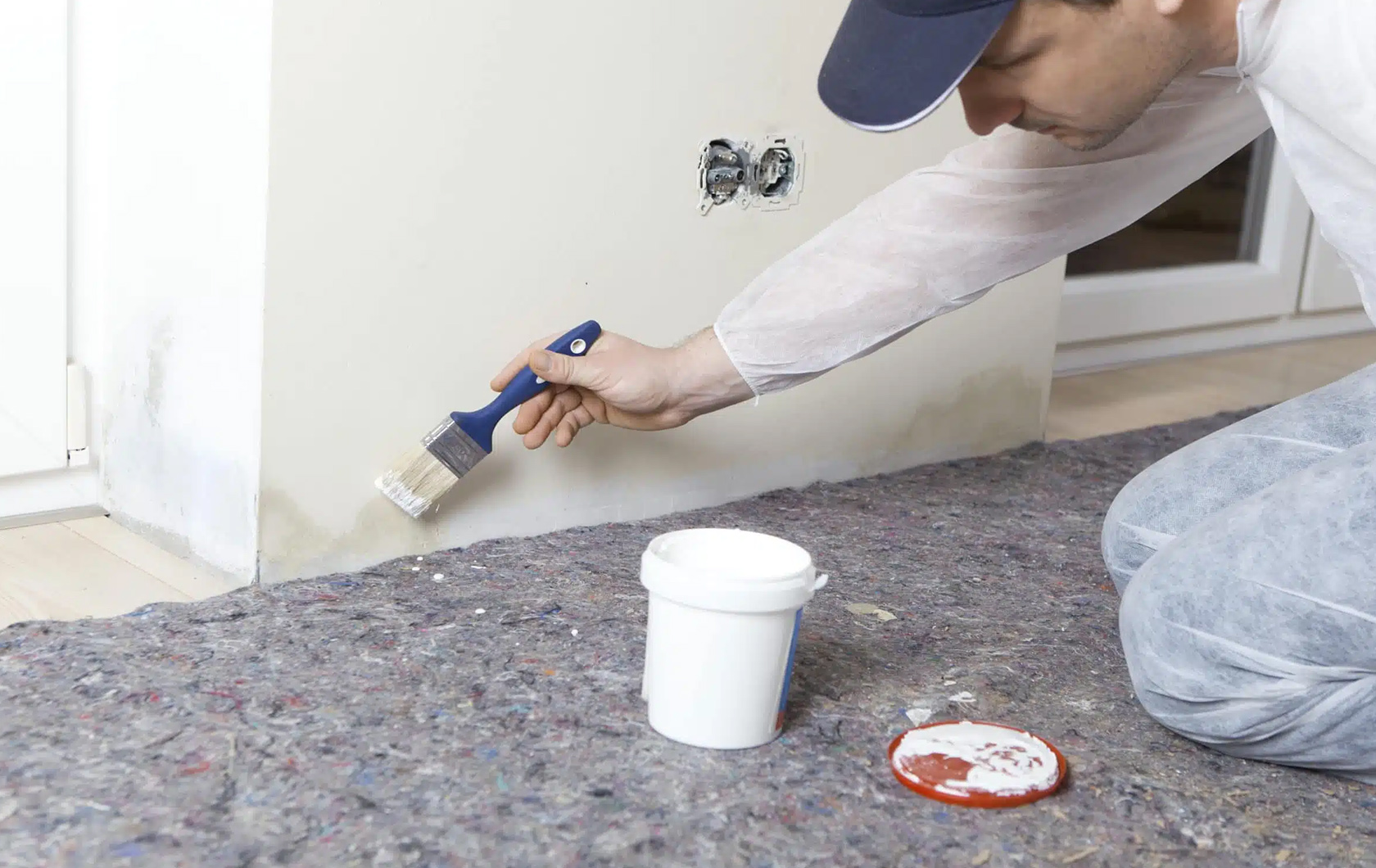 man painting the corner of a wall with white paint inside a home