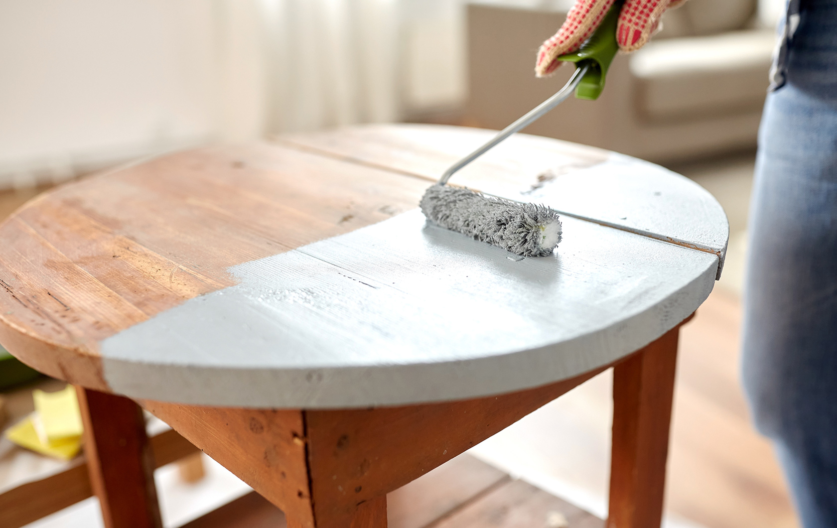 painting a wooden table with white paint using a paint roller