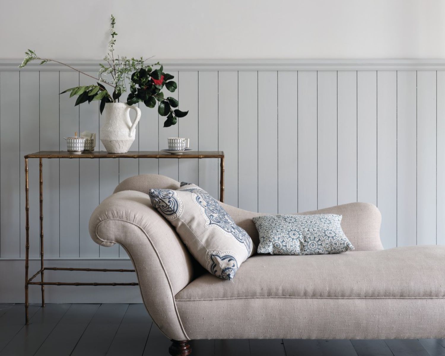 Farrow and Ball panelled wall painted in light blue-grey and wall painted in white, a light pink chaise longue and side table.